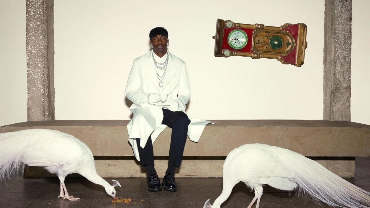 A figure in a white coat holds a teacup between two white peacocks beneath a sideways clock.