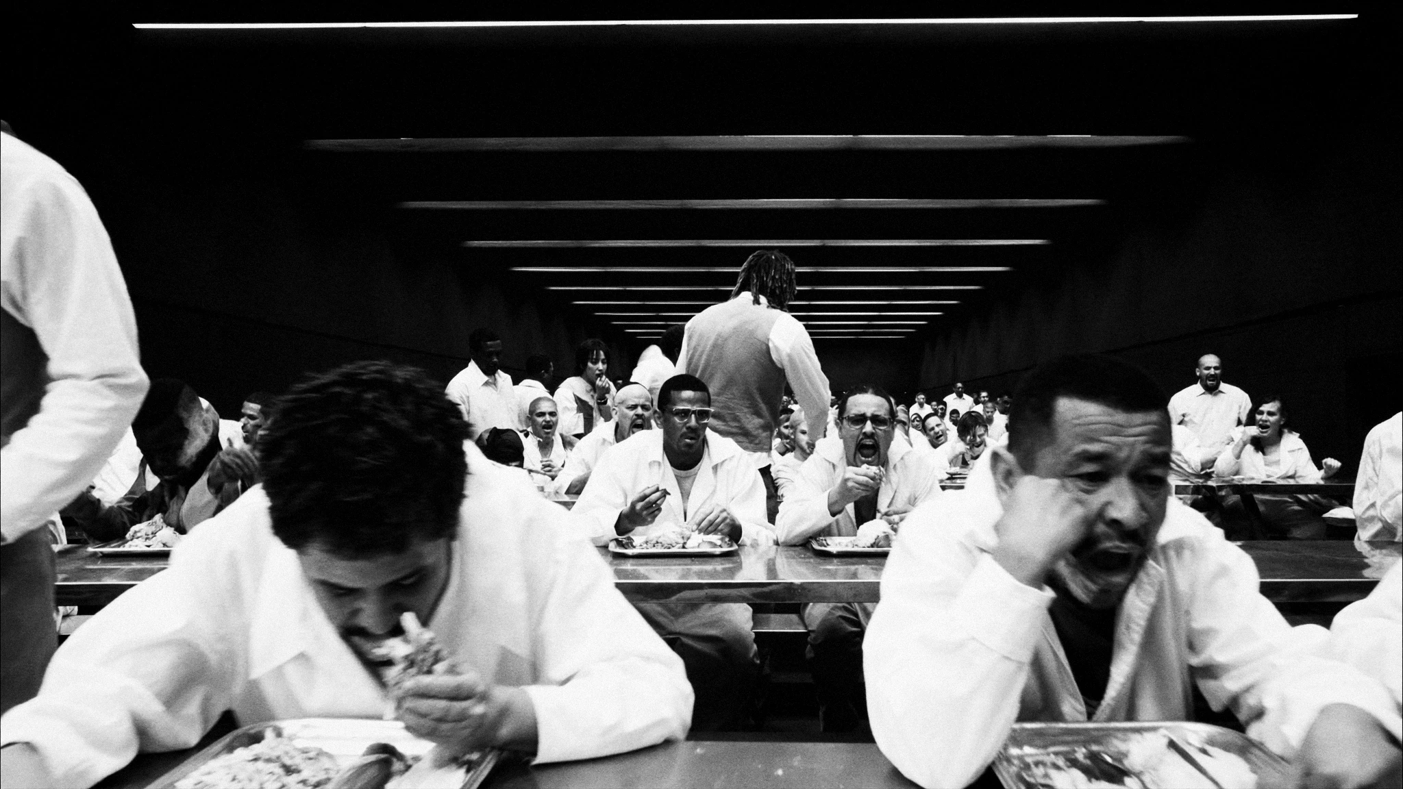 People dressed in white lean over tables in a dim communal room.