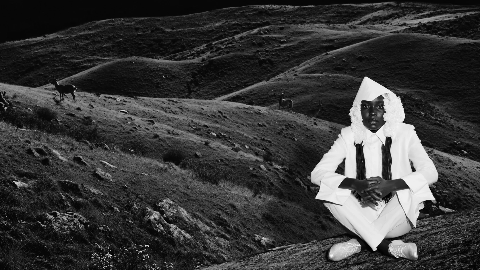 A cloaked white figure rests on a rocky hillside.