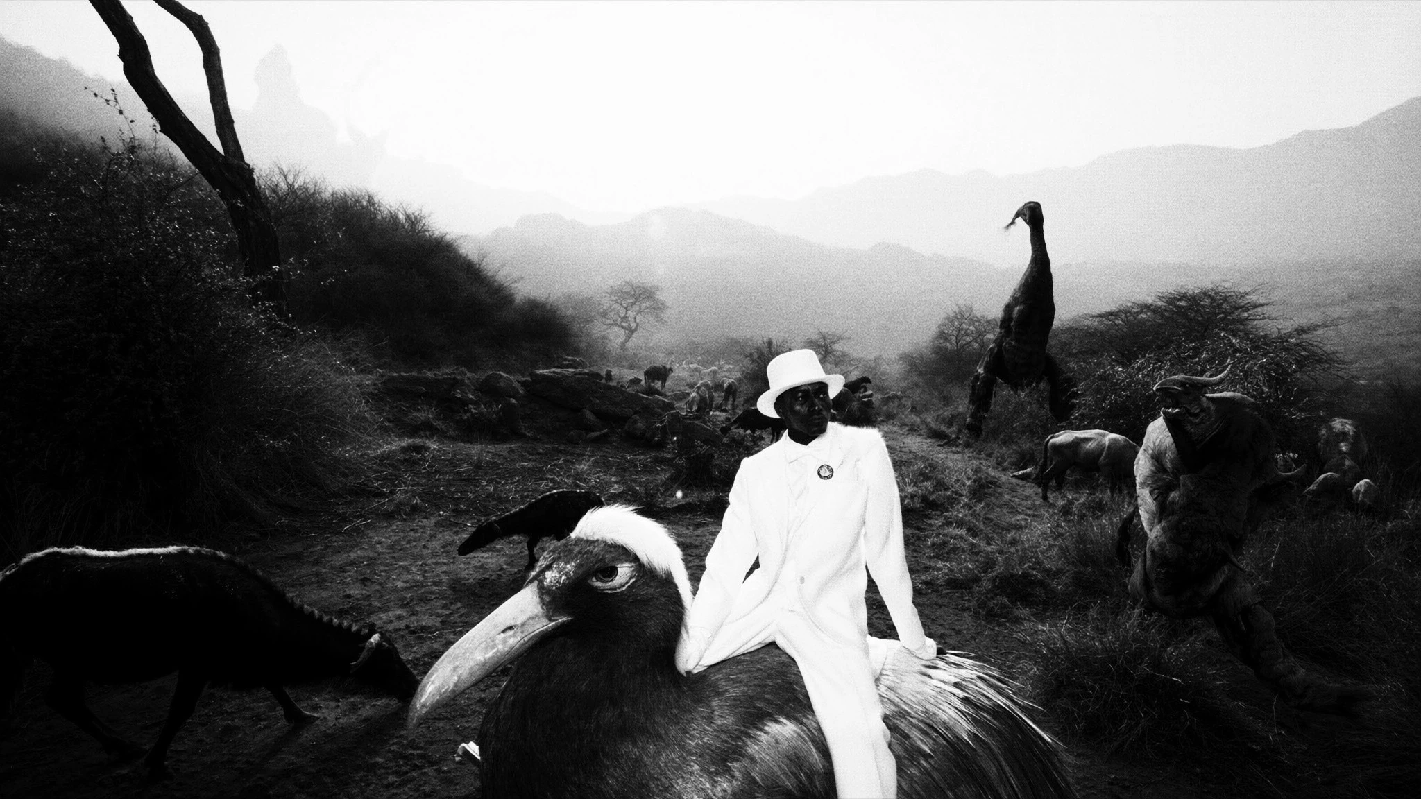 A man in white moves among strange creatures in an open mountain landscape.