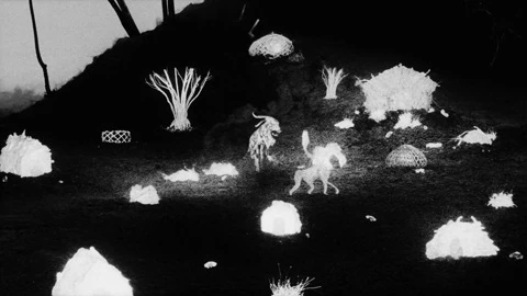 Figures gather around a small fire in the night.